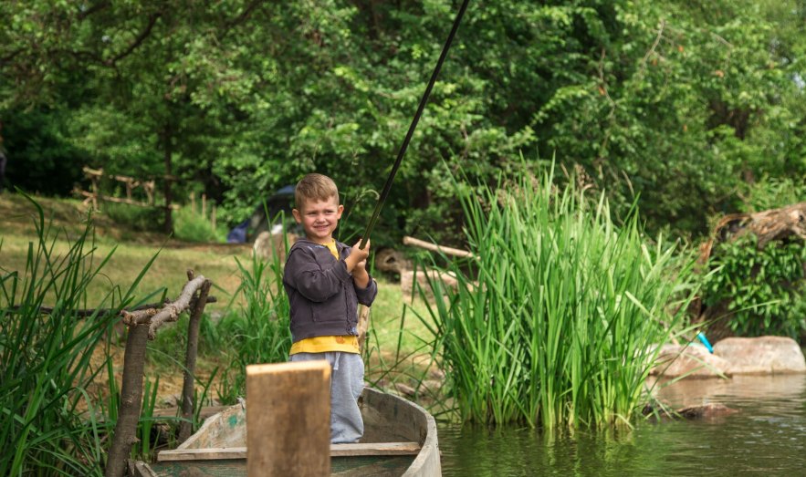 A young boy fishing from a small boat among tall green reeds