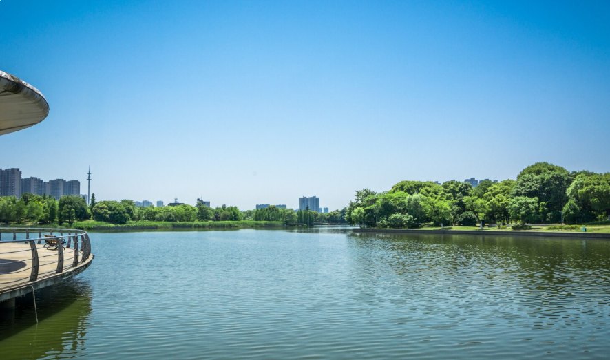 A calm blue lake with green trees and a city skyline in the distance
